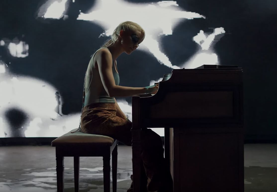 Meg Meyer sitzt an einem Klavier, im Hintegrund eine Videoleinwand mit schwarz-weißen Formen.