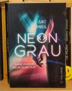 Paperback-Ausgabe von "Neongrau" mit Cover nach vorne im Regal stehend.