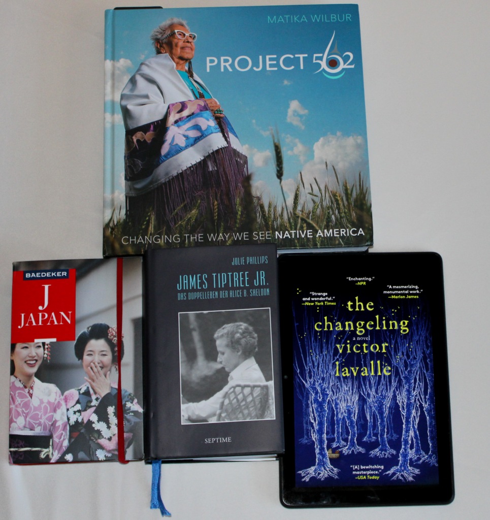 Drei Bücher und ein Tablet: Oben der Fotoband "Project 562". Untere Reihe von links nach rechts: Der Japan-Reiseführer von Baedecker, die Biografie von James Tiptree Jr. und auf dem Tablet der Roman "The Changeling".
