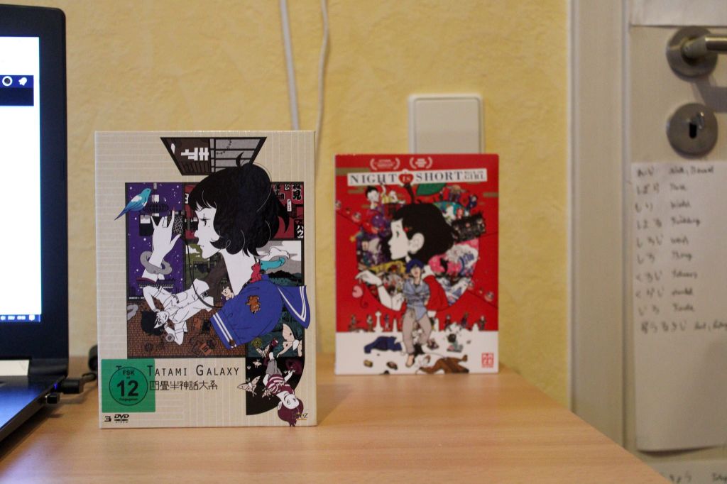 Foto der DVD-Box von "The Tatami Galaxy" aufrecht stehend auf einem Schreibtisch. Im Hintergrund leicht unscharft die DVD zu "Night is Short, Walk on Girl".