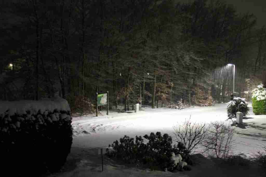 Das gleiche Motiv wie in den beiden Bildern zuvor, nur bei Nacht. Die schneebedckte Straße in der Mitte wird vom Licht einer Straßenlaterne erhellt.