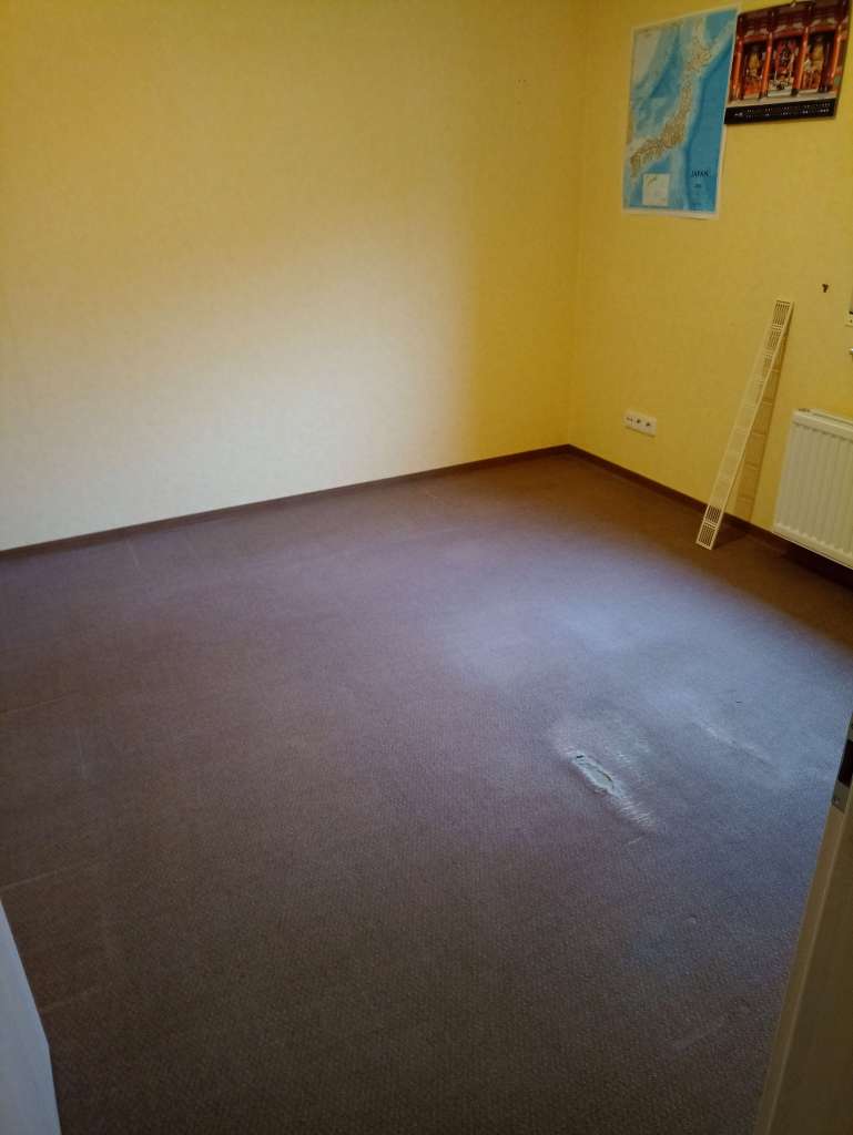 Mein leer geräumtes Arbeitszimmer, nur noch der alte braune Teppichboden mit einem größeren Loch in der Mitte ist zu sehen.