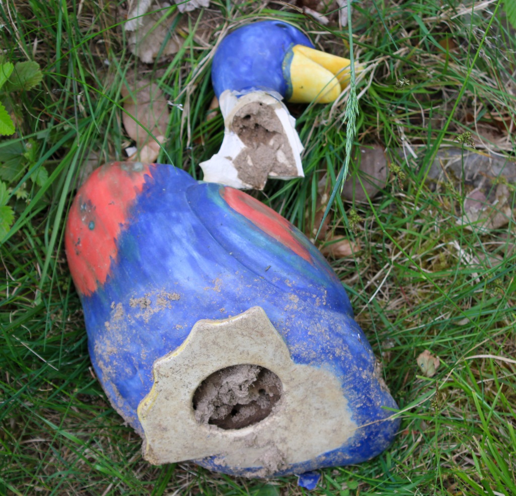 Eine auf der Seite liegende, blau bemalte Keramikente, deren Kopf abgebrochen ist. An der Bruchstelle, so wie an der Öffnung an der Unterseite ist zu sehen, das kleine Ameisen ihren Bau in die Ente hinein verlängert haben.